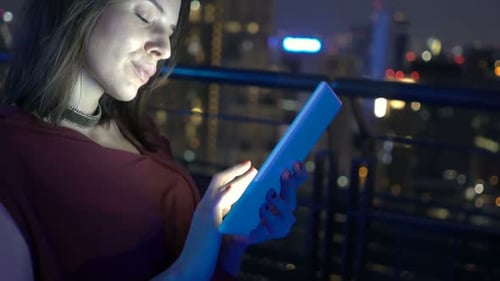 Young woman browsing internet on tablet at luxury rooftop bar terrace at night