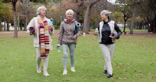Senior friends, walking and talking with yoga mats in the park to relax in nature with elderly women