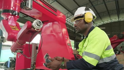 Black engineer test and control robotic arm in mechanical manufacturing factory.