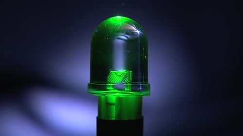 Soft zoom-in on a glowing green LED bulb with a dark background, highlighting the semiconductor chip