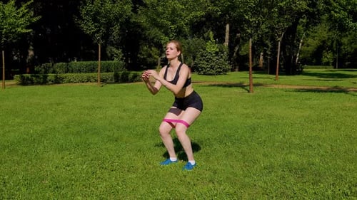 Woman Doing Squats with Resistance Band Outdoors