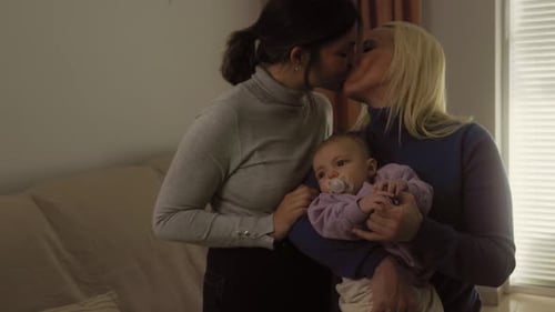 Happy lesbian couple having tender moments with their small baby at home