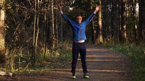 Fit Man in Athletic Wear Stretches Before a Morning Run on an Autumn Forest Trail Warming Up Muscles