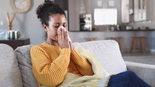 Woman with cold blowing her nose on couch