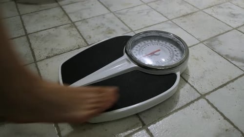 Old naked overweight and barefoot Woman measuring her Body Weight on Weighing Scales in a dark Bathr