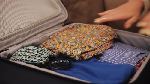 Woman packing colorful clothing into suitcase for travel