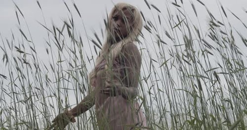 Ebony Girl In Pink Silk Gown Standing In Field Of Tall Grass On An Overcast Summer Day. Medium Shot.