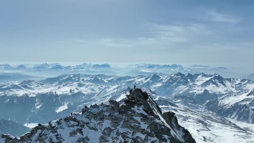 Drone shot of a person standing on a rocky peak in the Alps.