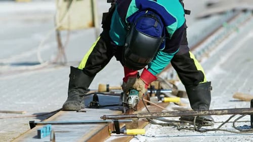 Arbeiter schleift Bahngleise mit Elektrowerkzeug in Zeitlupe auf der Baustelle