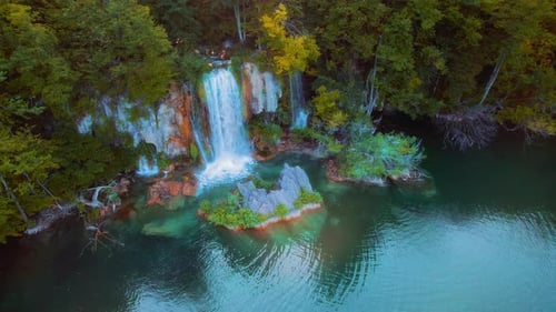 Mountain forest landscape with powerful waterfall at sunset. Green deciduous trees and dark water of