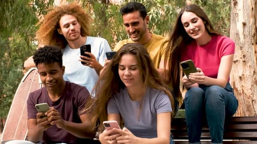 Group friends holding mobile phones watching videos online, chatting at street.