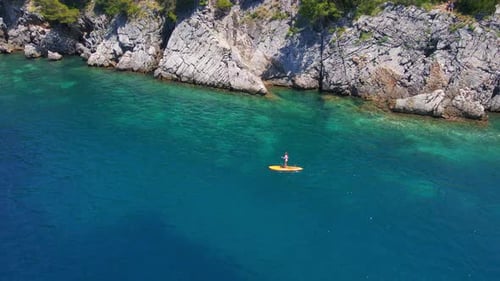 Young Woman on a Stand Up Paddle Board SUP Rawing Among Beatyful Rocks