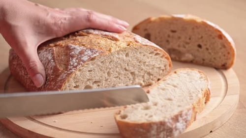 Woman cutting bread on cutting board at the kitchen.
