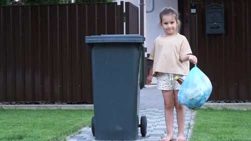 Portrait of a Little Girl with a Garbage Bag Near a Trash Can