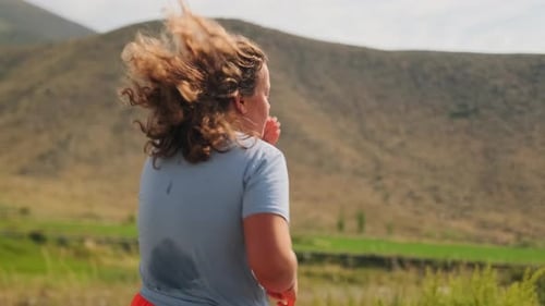 Teenage Girl Runs Across a Field Wiping Sweat As the Wind Blows