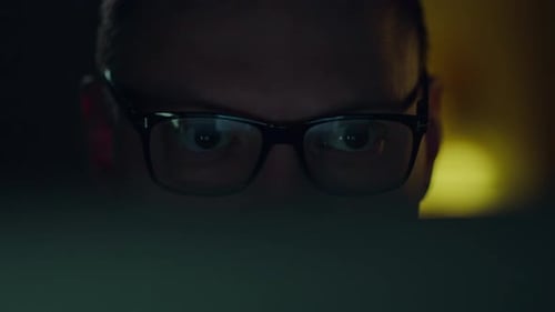 Evening working hours of an IT programmer, close-up reflection of the monitor in his glasses