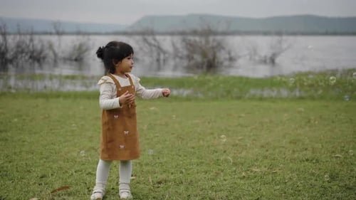 slow motion of happy toddler girl playing soap bubble in grass field near the river