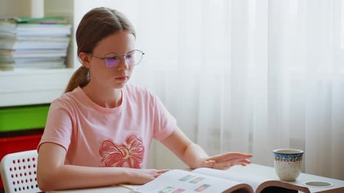 Girl Studies Textbook at Table Indoors