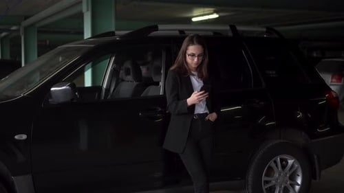 Young Business Woman Standing By the Car in the Parking Lot with a Phone in Her Hand