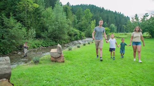 Young happy family walks on grass in park near water stream, Slovenia