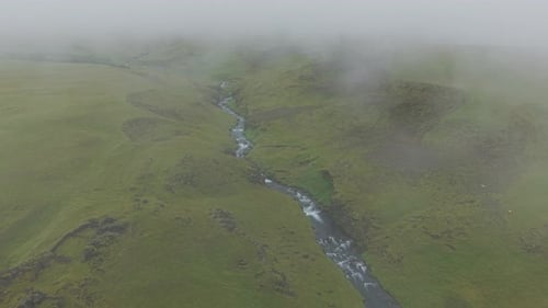 Aerial backwards shot revealing a vast mossy volcanic canyon and river