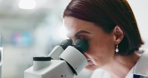 Woman Looks Through Microscope in Bright Lab