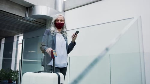 Senior woman waits at airport gate wearing face mask during coronavirus pandemic