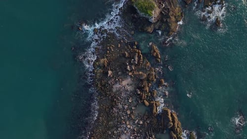 Drone shot of Atlantic Ocean waves crashing against the dark rocks of Armação Beach. High-contrast