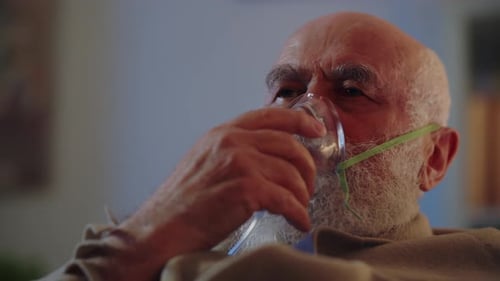 Un homme âgé malade qui se soigne à domicile de façon autonome utilise un masque à oxygène pour faciliter la respiration et se couvre