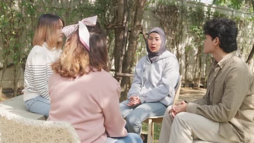 Small Asian group of people sit in a close circle and talk to a therapist in park.