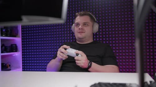 Gamer Sits at Table and Plays Console in Studio Enthusiastic Man with Joystick in His Hands Plays