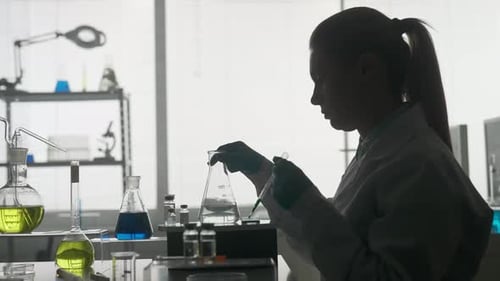 Dark Silhouette of a Female Scientist A Woman Using a Pipette Will Add a Green Reagent to a Glass