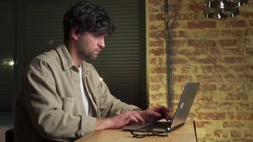 Young Adult Man Typing on Laptop at Table