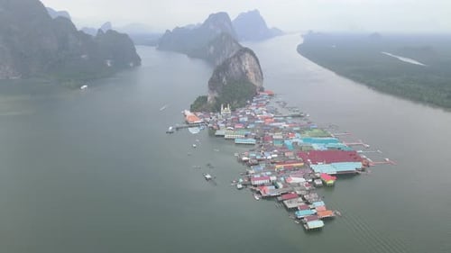 Fly from left to right aerial view of Panyee island and village with cloudy sky and some boat sail