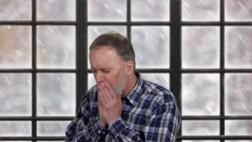 Man Warming Hands Indoors During Snowfall