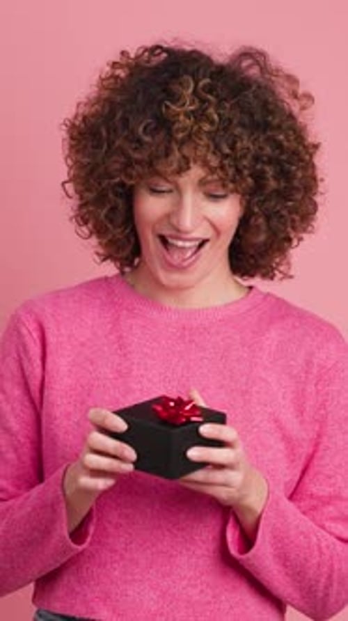 Surprised Woman Opening Gift Box in Pastel Pink Colored Studio Vertical Footage