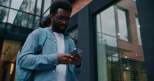 African American Student Walking Away From Campus Checking Something on Mobile Phone and Exclaiming