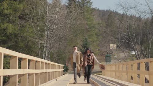 Couple Running Hand-in-Hand on a Wooden Bridge