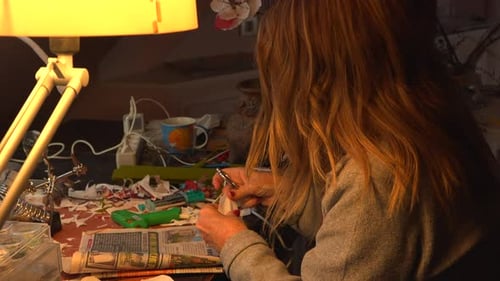 Woman Crafting Underneath Lamp Light at Desk