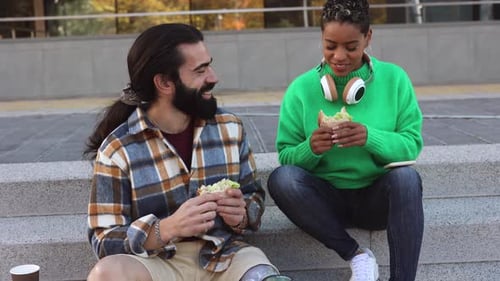 multiracial couple eating a sandwich outdoors in the street