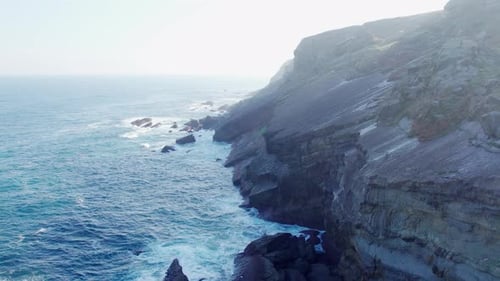 Drone aerial flying along a rocky Coastline alongside Cliffside ridges with Blue Ocean Water Towards
