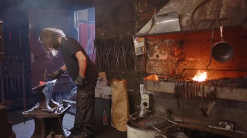 Blacksmith Hammering Hot Metal in Dark Workshop