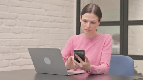 Woman Using Laptop and Smartphone at Desk