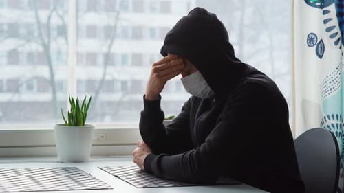 Person in Mask Sits Indoors by a Window
