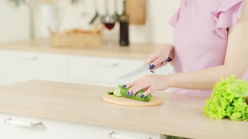 Woman Slices Cucumber on a Cutting Board in Kitchen