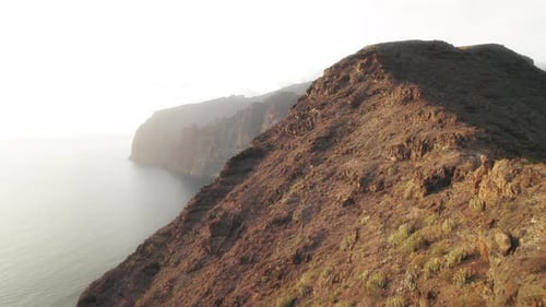 Person stands on a rocky outcrop, arms outstretched, embracing the sunset over the ocean with Los Gi