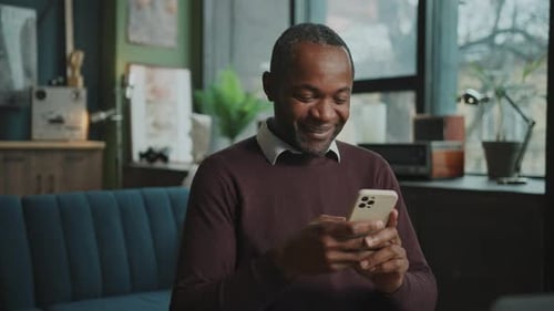 Man Using Smartphone, Smiling Sitting on Couch Indoors