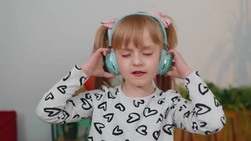 Happy Child Girl Kid in Headphones Dancing and Jumping While Listening to the Music at Home Alone