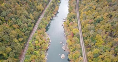 Slow aerial pan along an autumnal forest with a river flowing in between