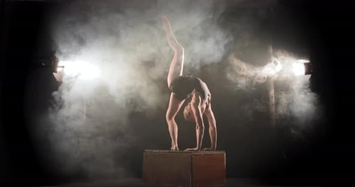 Acróbata doblado hacia atrás en el palco levantando la pierna, actuación en el escenario con focos llenos de humo